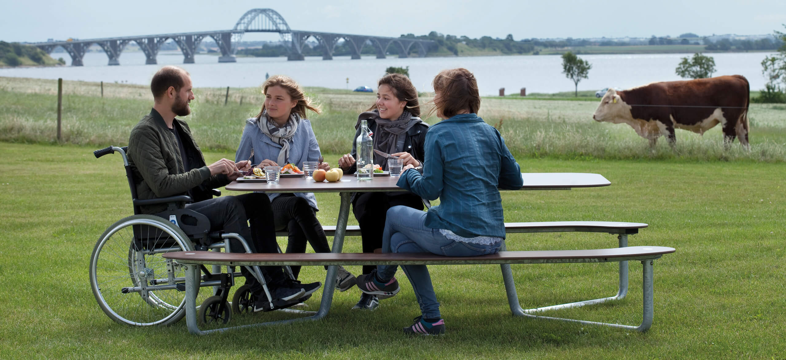 Et plateau picnic I bord i grønne omgivelser, hvor fire personer spiser frokost