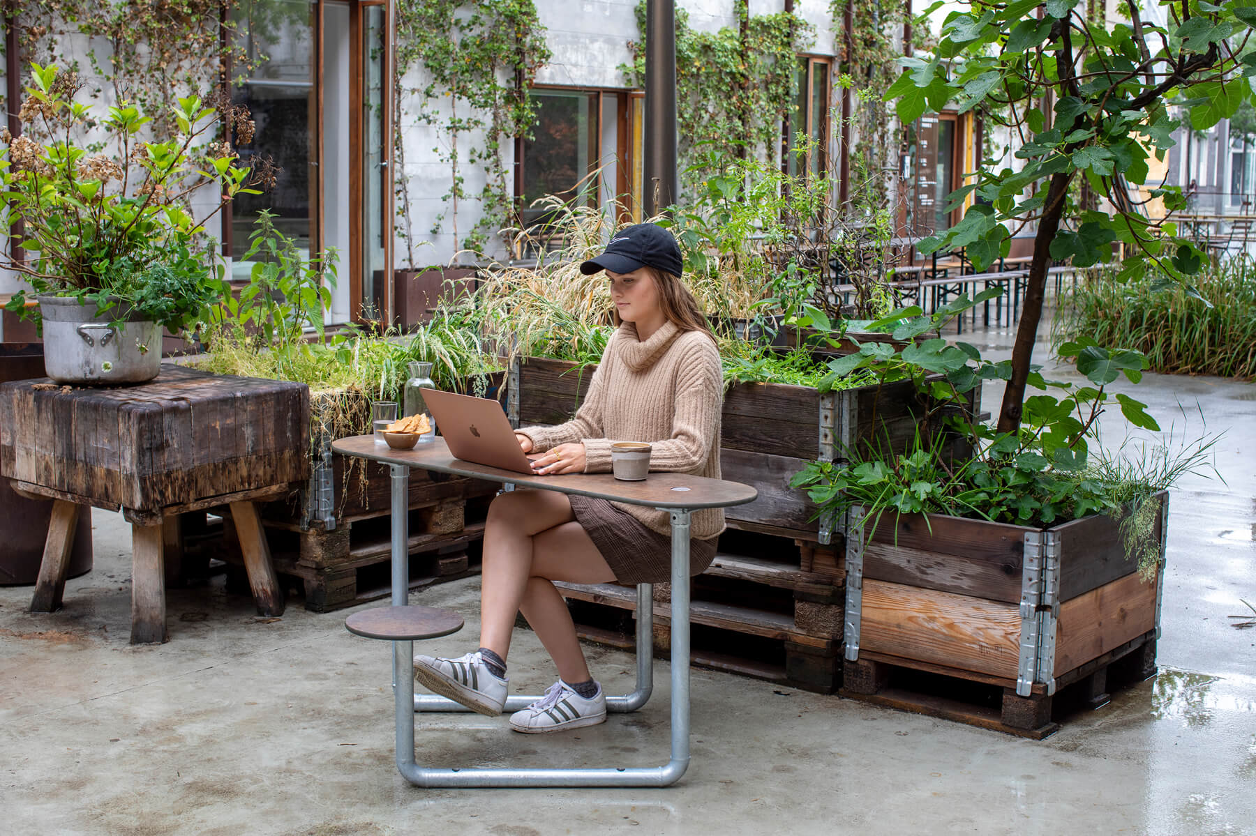 En kvinde der bruger sin computer på en cafe. Hun sidder på et brunt Plateau Picnic Duo bordbænkesæt