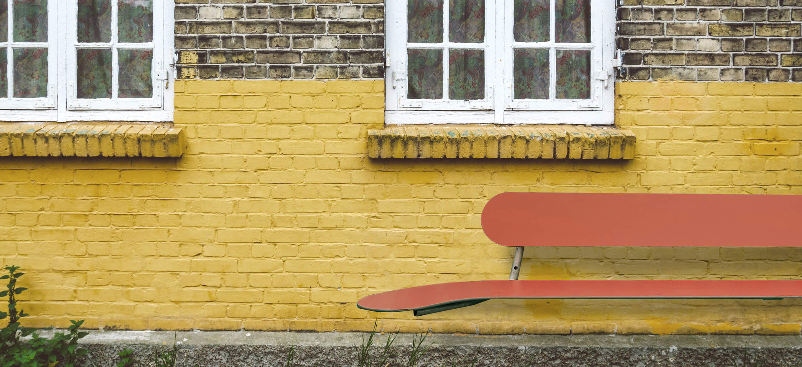 En Plateau vægbænk i farven terracotta op ad en gul mur
