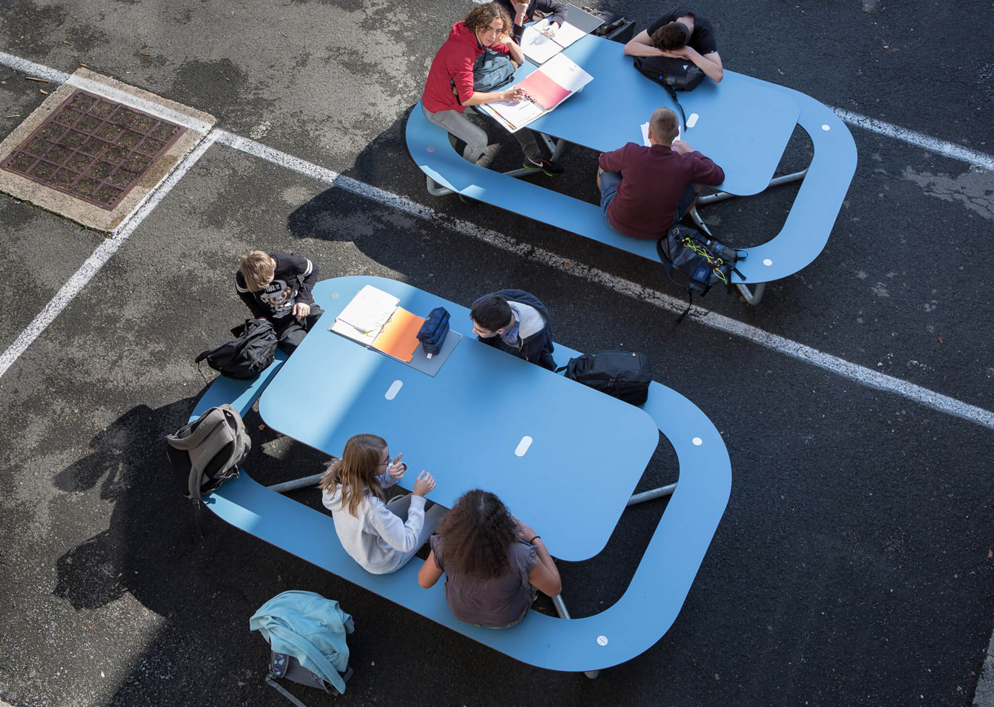 Oppe fra billede af et blåt PLATEAU Picnic O bordbænkesæt i en skolegård, hvor børn arbejder med deres computere