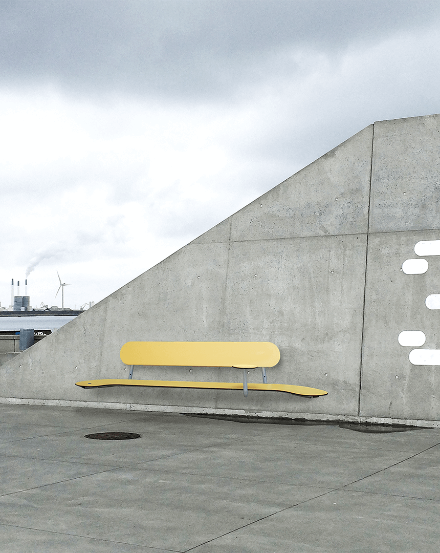 En vægbænk i gul monteret op ad en betonmur på Amagerstrand